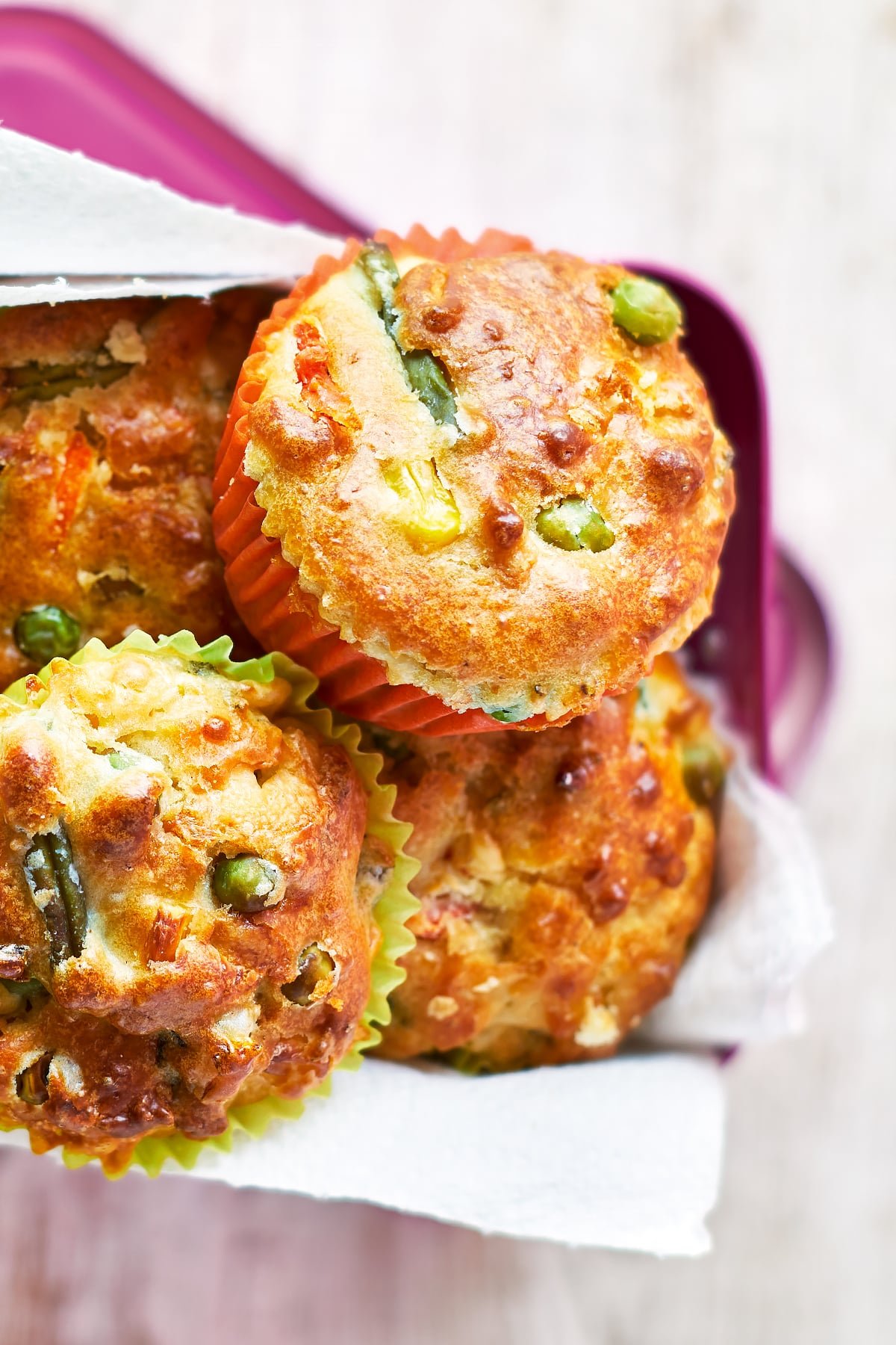 Savoury vegetable muffins in a pink lunchbox lined with paper. The muffins are in multicoloured cases.