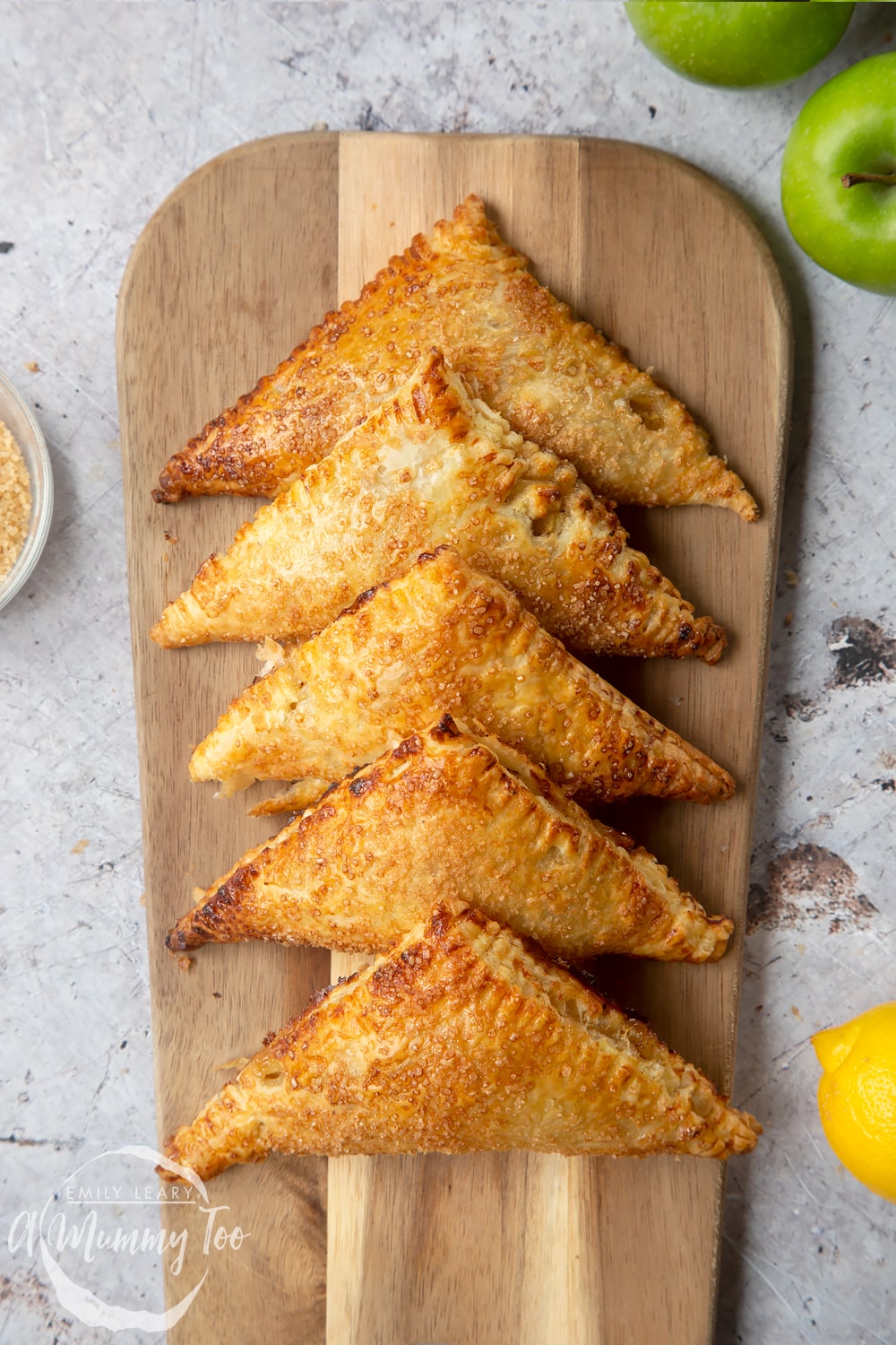 Overhead shot of five cinnamon apple turnovers lined up on a wooden chopping board.