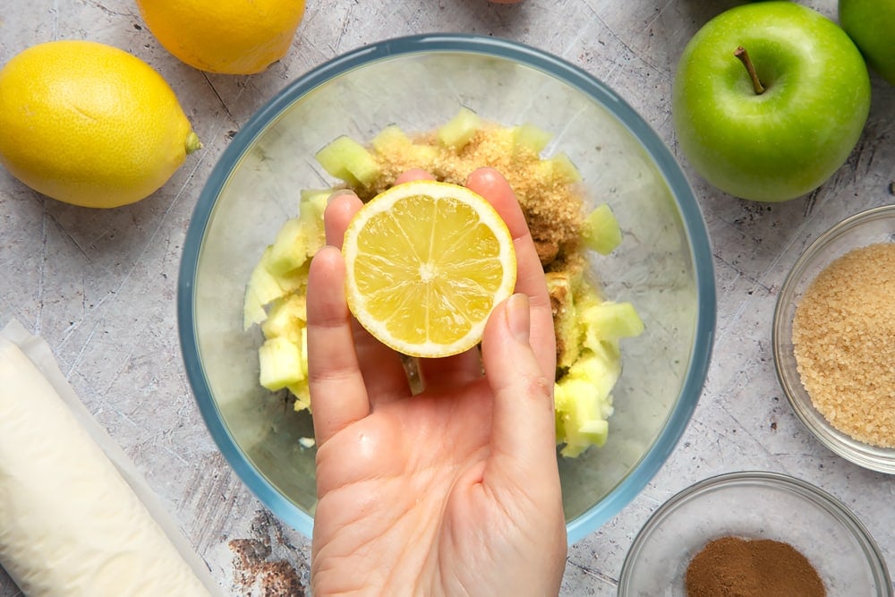 Overhead shot of a hand holding a lemon over a bowl of ingredients and fruit