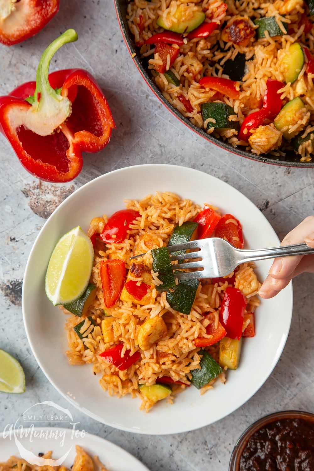 Overhead shot of hand holding a fork picking up Spicy BBQ halloumi rice side served on a white bowl with a mummy too logo in the lower-left corner