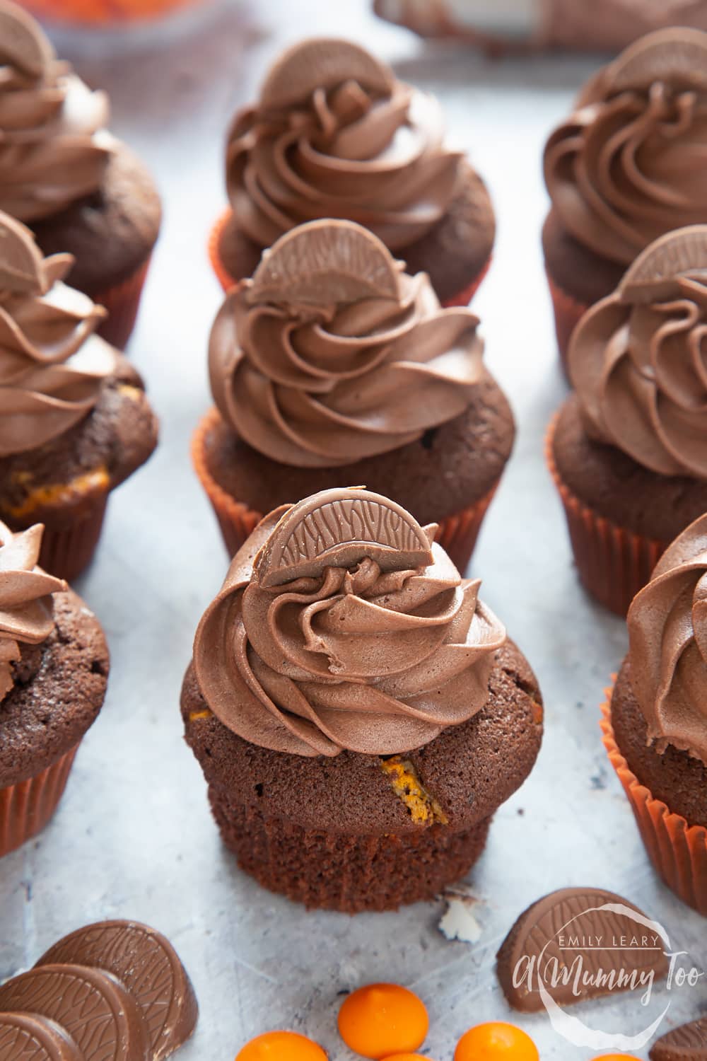 Front angle shot of chocolate orange muffins topped with colourful chocolate orange chips with a mummy too logo in the lower-right corner