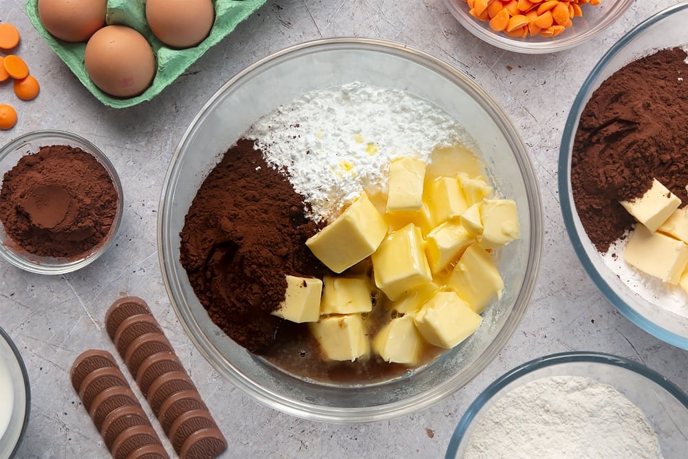 Overhead shot of butter, icing sugar, cocoa powder, hot water and orange essence in a large mixing bowl