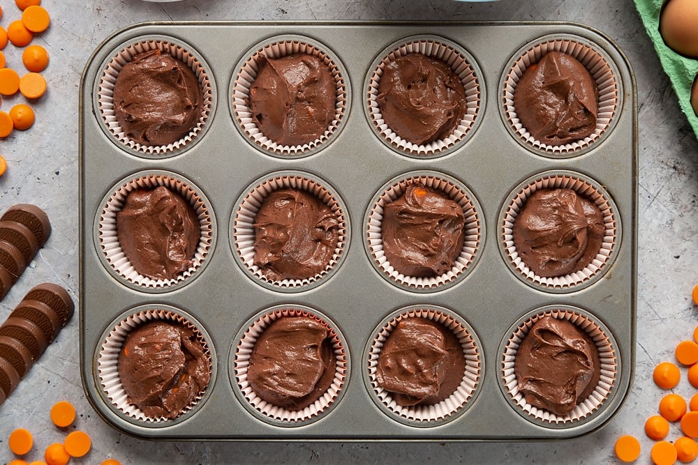 Overhead shot of chocolate orange muffin batter in muffin tray with muffin cases