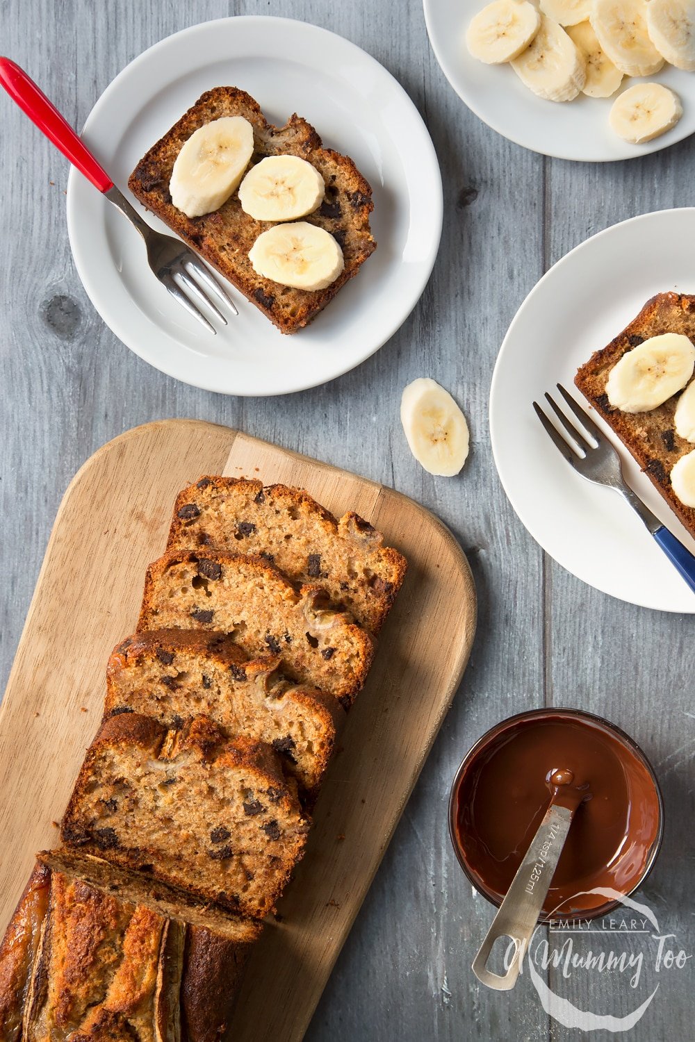 Overhead shot of dark chocolate banana loaf slices on two white plates with the remaining loaf on a wooden board.