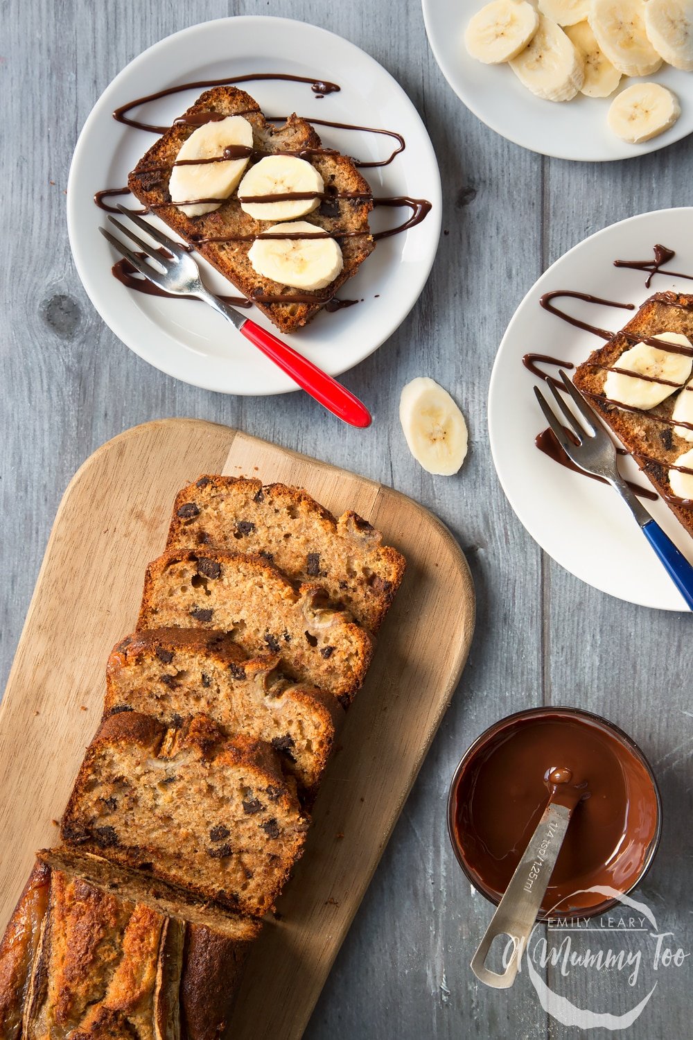 Overhead shot of dark chocolate banana loaf slices on two white plates with the remaining loaf on a wooden board.