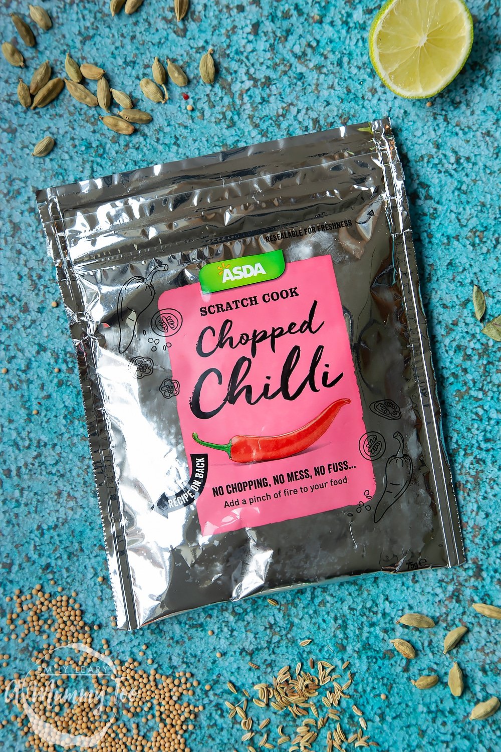 A sachet of frozen chopped chilli on a blue background, surrounded by curry ingredients.