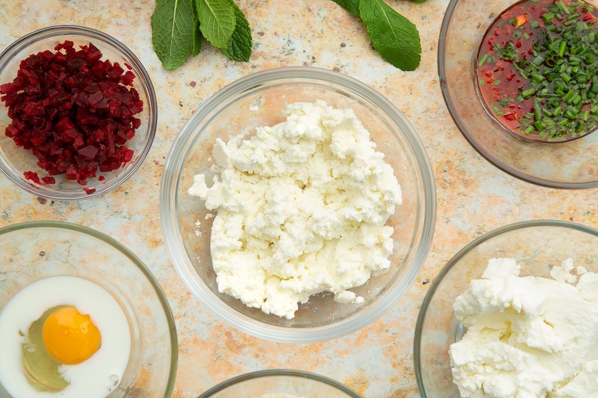 Mashed goat's cheese in a mixing bowl. Ingredients to make goat's cheese croquettes surround the bowl.