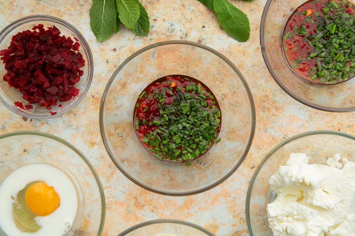 Chives, maple syrup and chopped red chilli in a glass bowl. Ingredients to make goat's cheese croquettes surround the bowl.