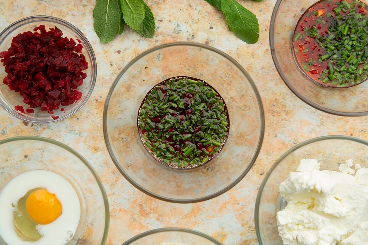 Chive, maple syrup and red chilli dressing in a glass bowl. Ingredients to make goat's cheese croquettes surround the bowl.