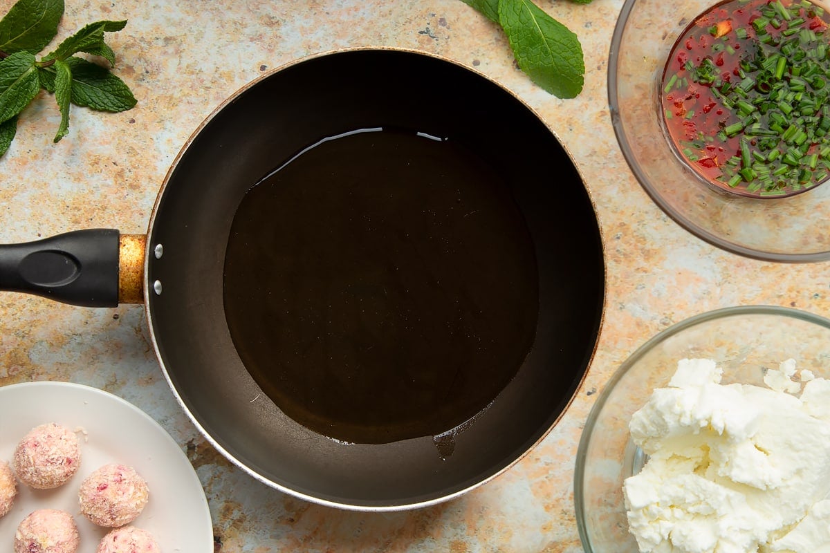 A frying pan with oil. Ingredients to make goat's cheese croquettes surround the pan.