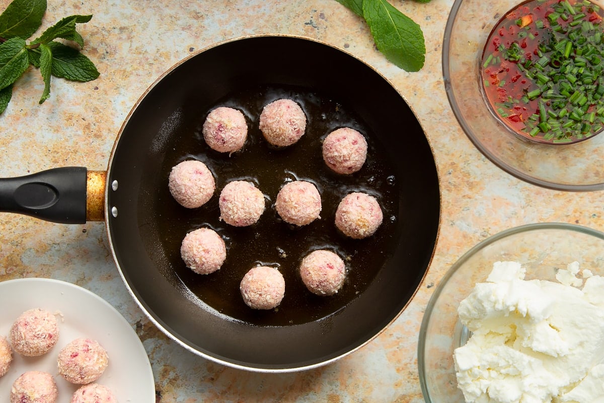 Goat's cheese and beetroot croquettes in a frying pan. Ingredients to make goat's cheese croquettes surround the plate.