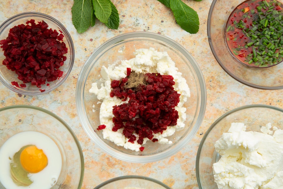 Mashed goat's cheese in a mixing bowl with chopped beetroot. Ingredients to make goat's cheese croquettes surround the bowl.