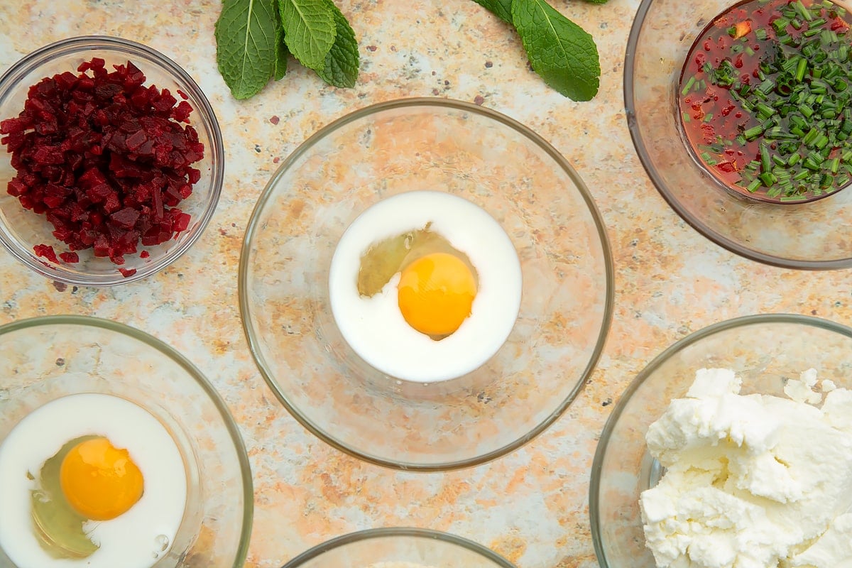 Egg and milk in a small glass bowl. Ingredients to make goat's cheese croquettes surround the bowl.