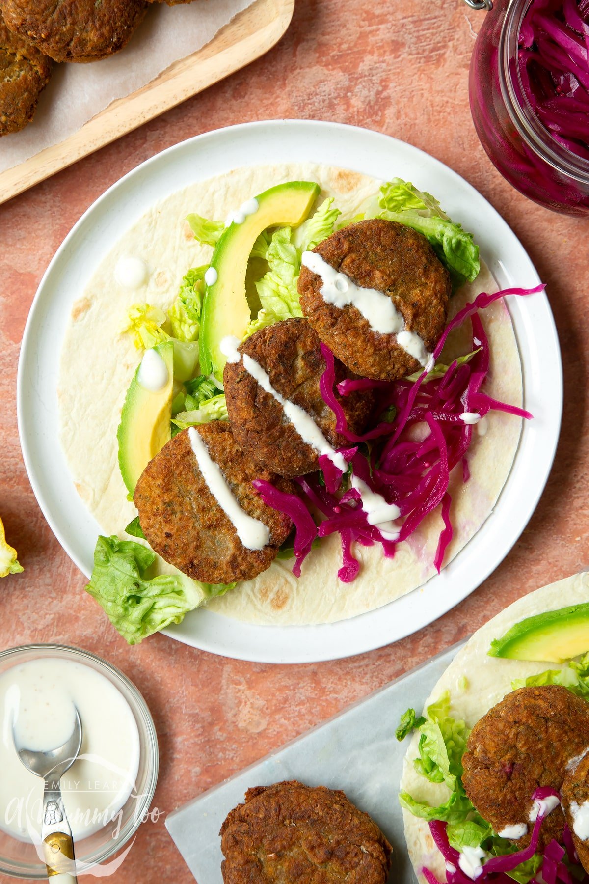 A harissa falafel wrap arranged on a plate with pickled cabbage and salad, drizzled with tahini dressing.