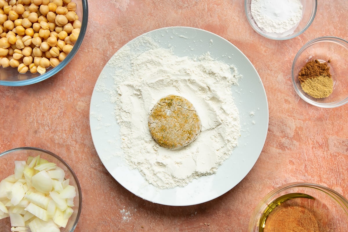 A harissa falafel patty on a plate of flour.