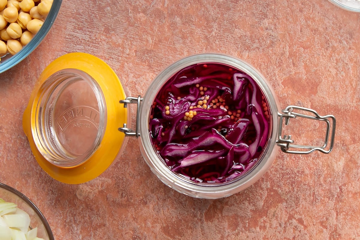 A preserving jar containing thinly sliced shallots and red cabbage, covered with pickling liquor.