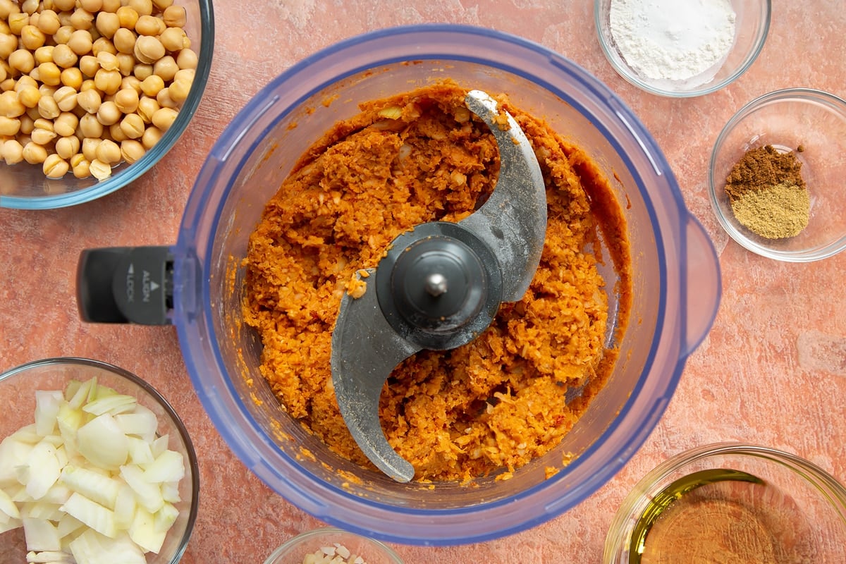 A food processor containing a harissa falafel paste made from chickpeas, spices, garlic, flour, baking powder and chopped onion.