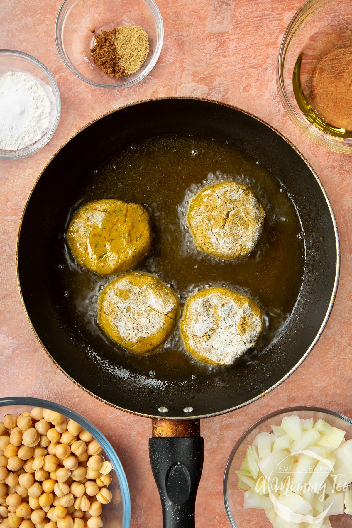 Four harissa falafel patties shallow frying in a pan.