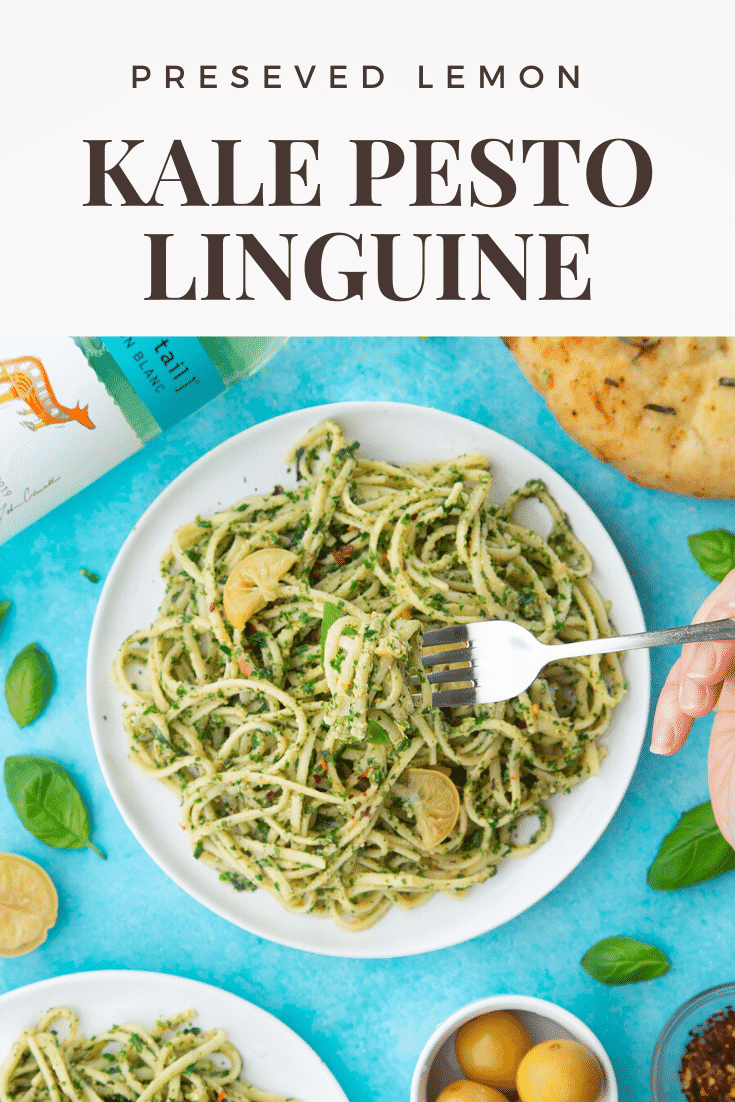 A white plate with kale pesto linguine, topped with basil and slices of preserved lemons. A hand holds a fork, lifting some pasta. A caption reads: preserved lemon kale pesto linguine.