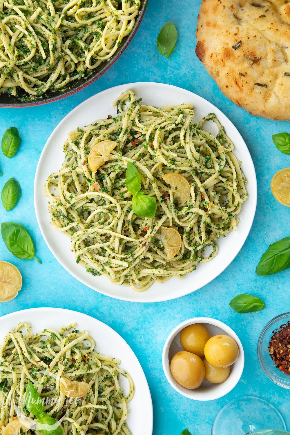 Two white plates with kale pesto linguine, topped with basil and slices of preserved lemons. 