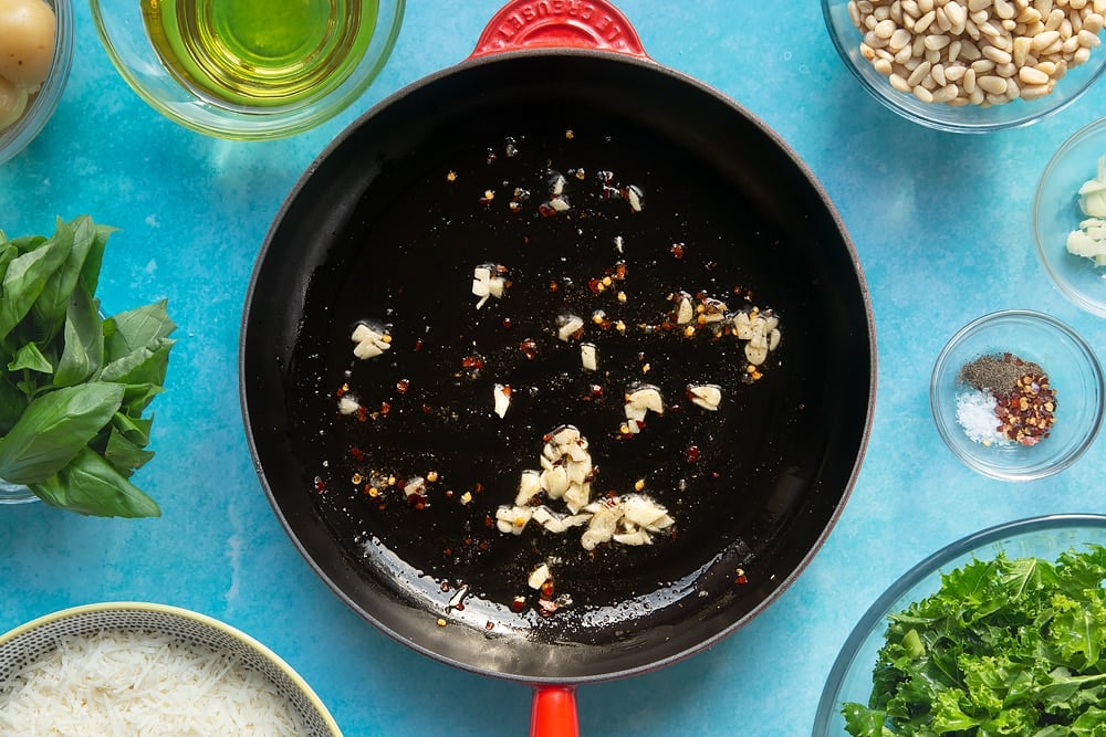 A pan containing fried garlic, chilli salt and pepper. The pan is surrounded by ingredients for kale pesto linguine.