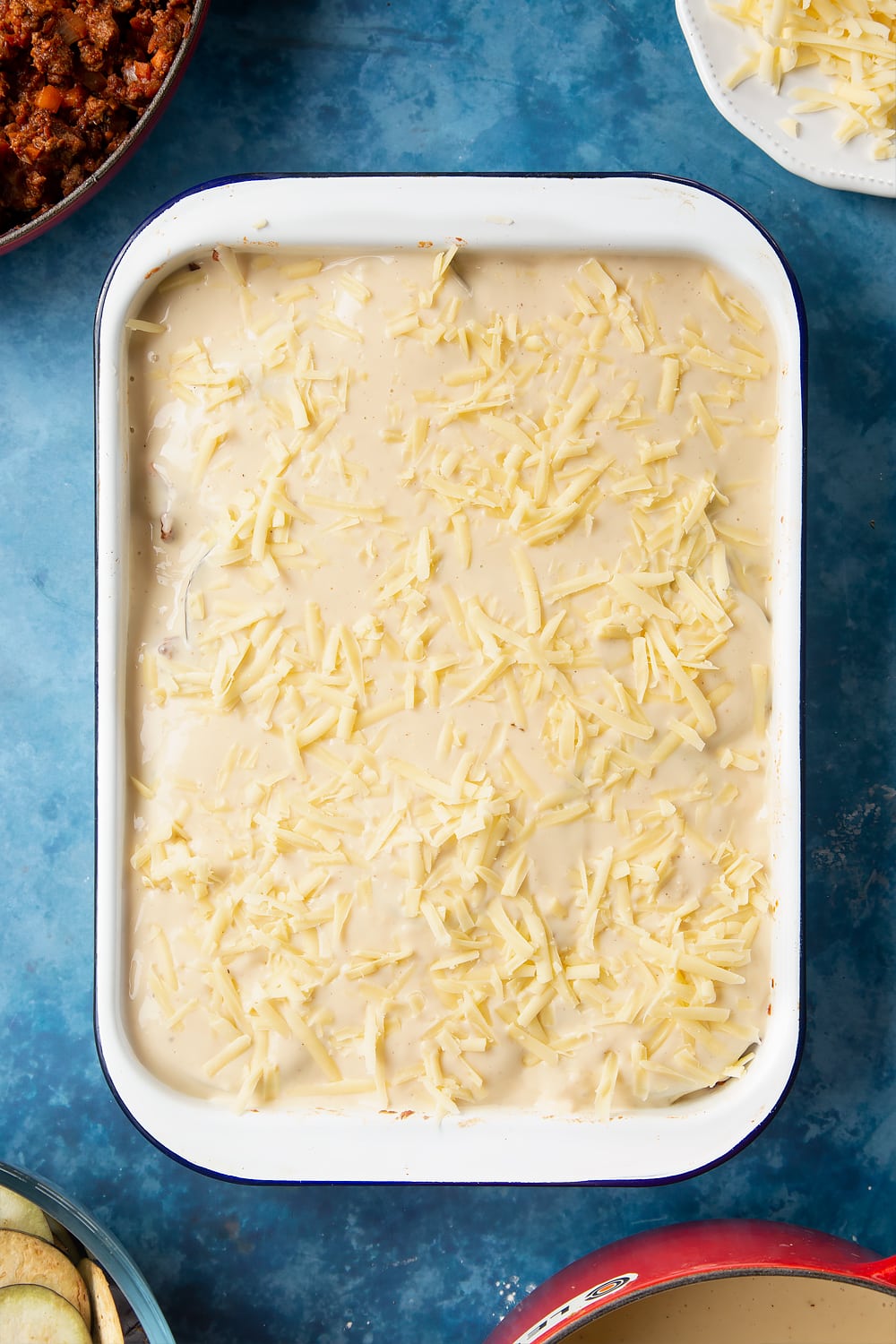 Overhead shot of quorn meat free mince moussaka covered with white sauce topped with grated cheese on a large white roasting tray