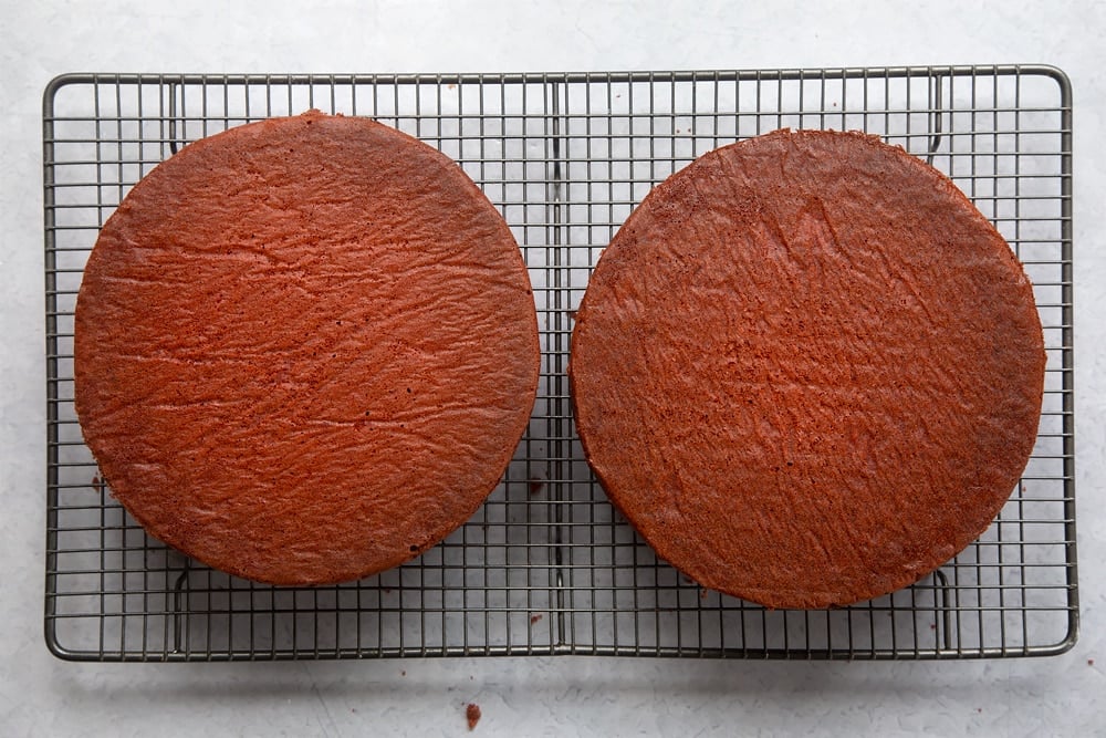 Two cooked red velvet sponges on. a cooling rack.