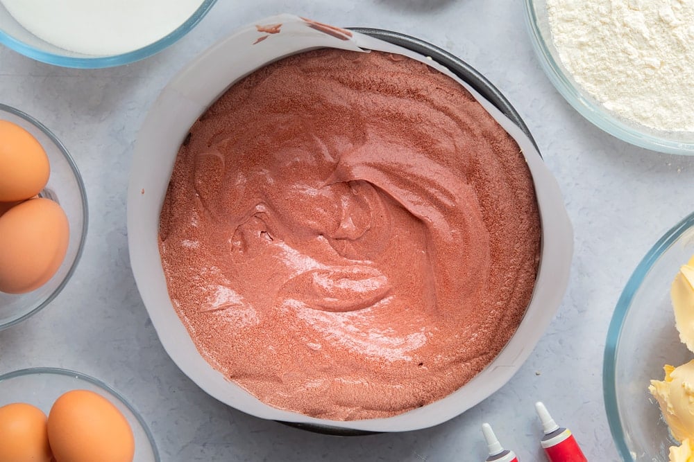 Red velvet cake batter in sandwich tin. Ingredients to make filled red velvet cake surround the tin. 