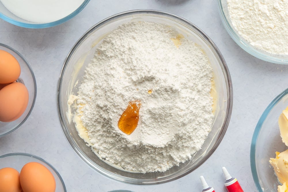 Margarine, cream cheese, icing sugar and vanilla extract in a large glass mixing bowl. Ingredients to make filled red velvet cake surround the bowl. 