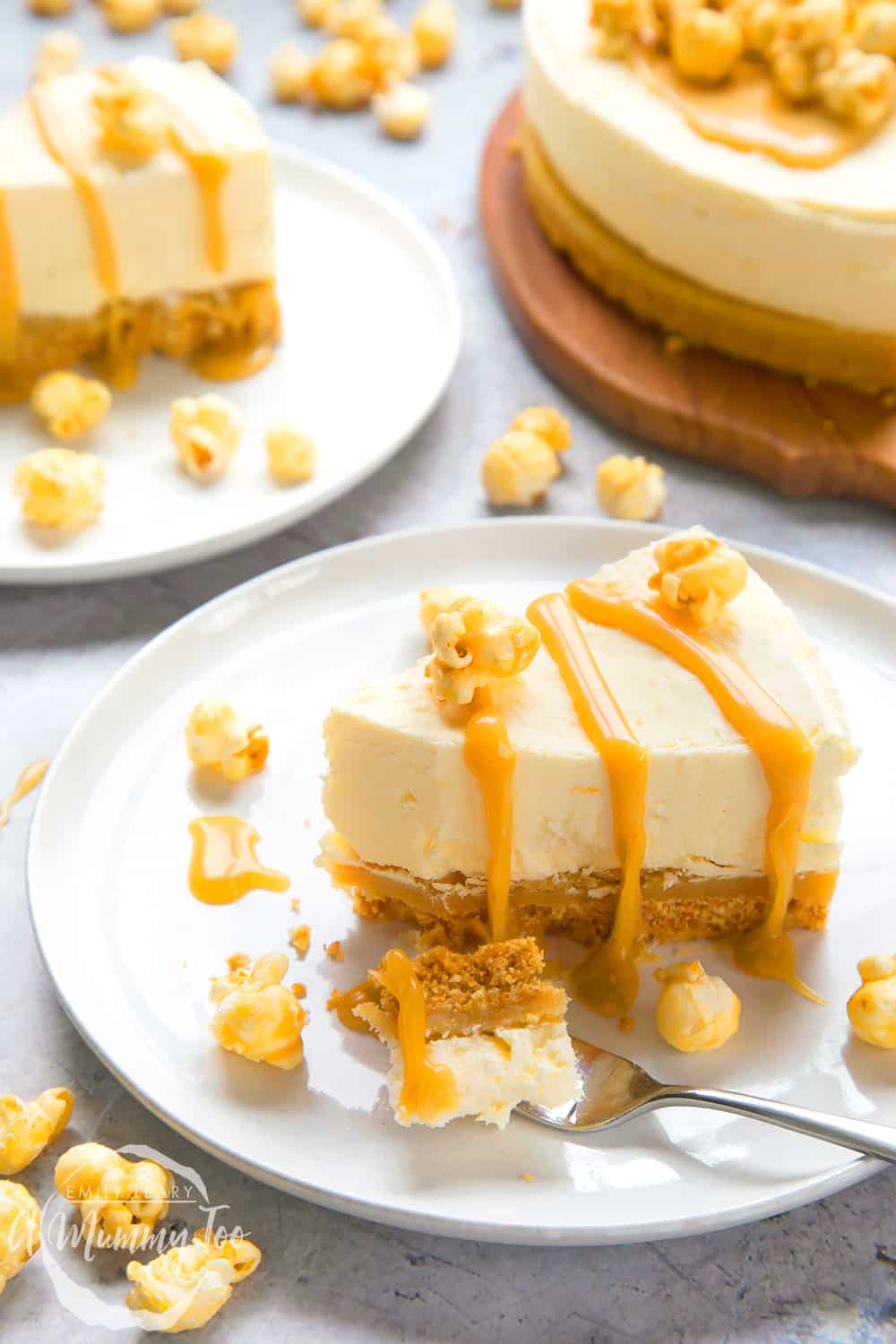 a slice of no-bake salted caramel cheesecake drizzled with caramel sauce and topped with popcorn on a white plate and a fork cutting a piece away.