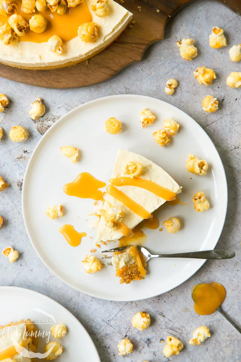 over head view of a slice of no-bake salted caramel cheesecake drizzled with caramel sauce and topped with popcorn on a white plate and a fork cutting a piece away.