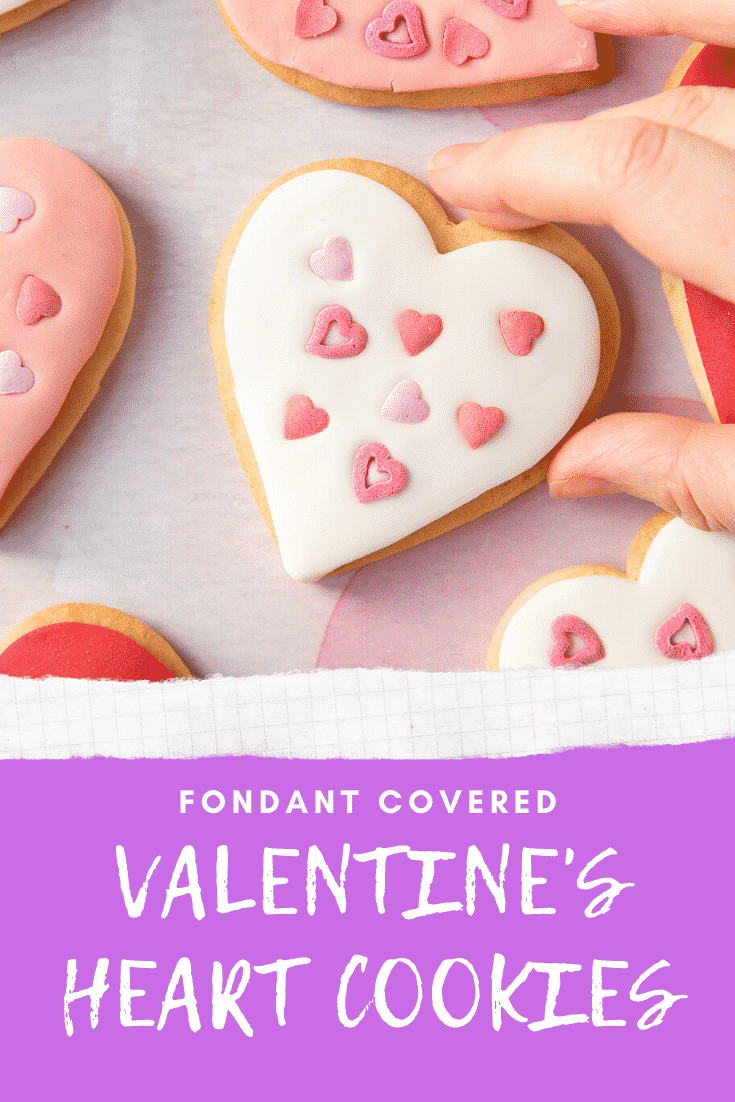 graphic text FONDANT COVERED VALENTINE'S DAY COOKIES above an Overhead shot of a hand holding a valentines day cookies