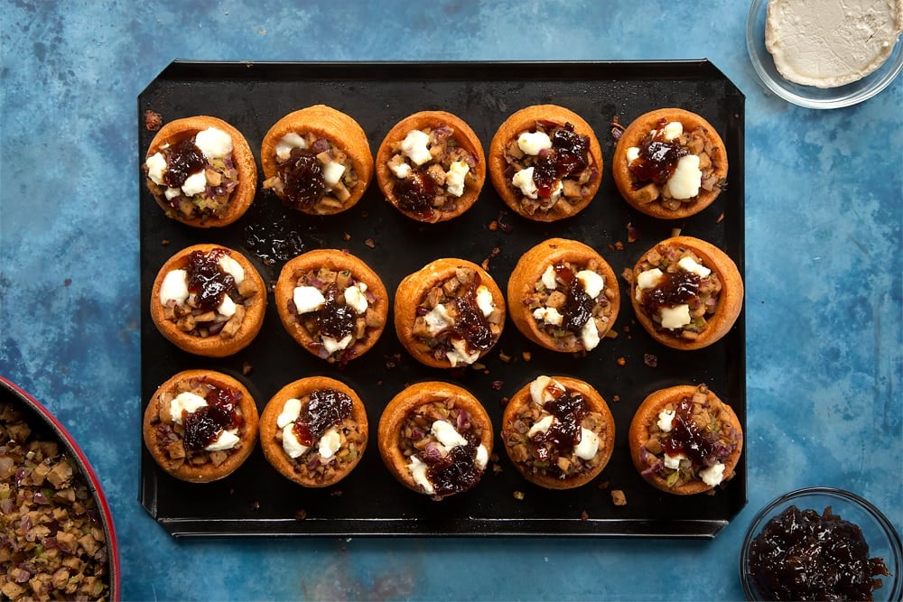 baked mini yorkshire puddings on a lined baking tray topped with cooked stuffing mix with goats cheese.