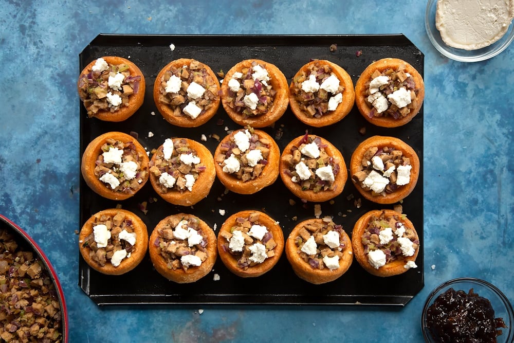 mini yorkshire puddings on a lined baking tray topped with cooked stuffing mix with goats cheese.