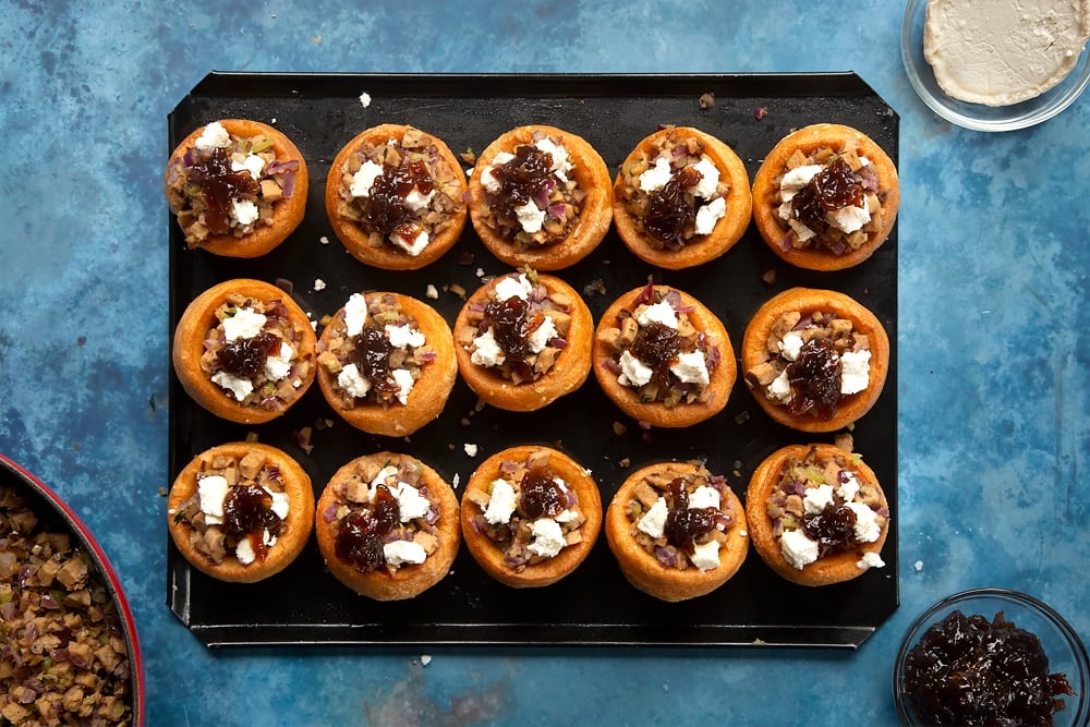 mini yorkshire puddings on a lined baking tray topped with cooked stuffing mix with goats cheese and chutney.