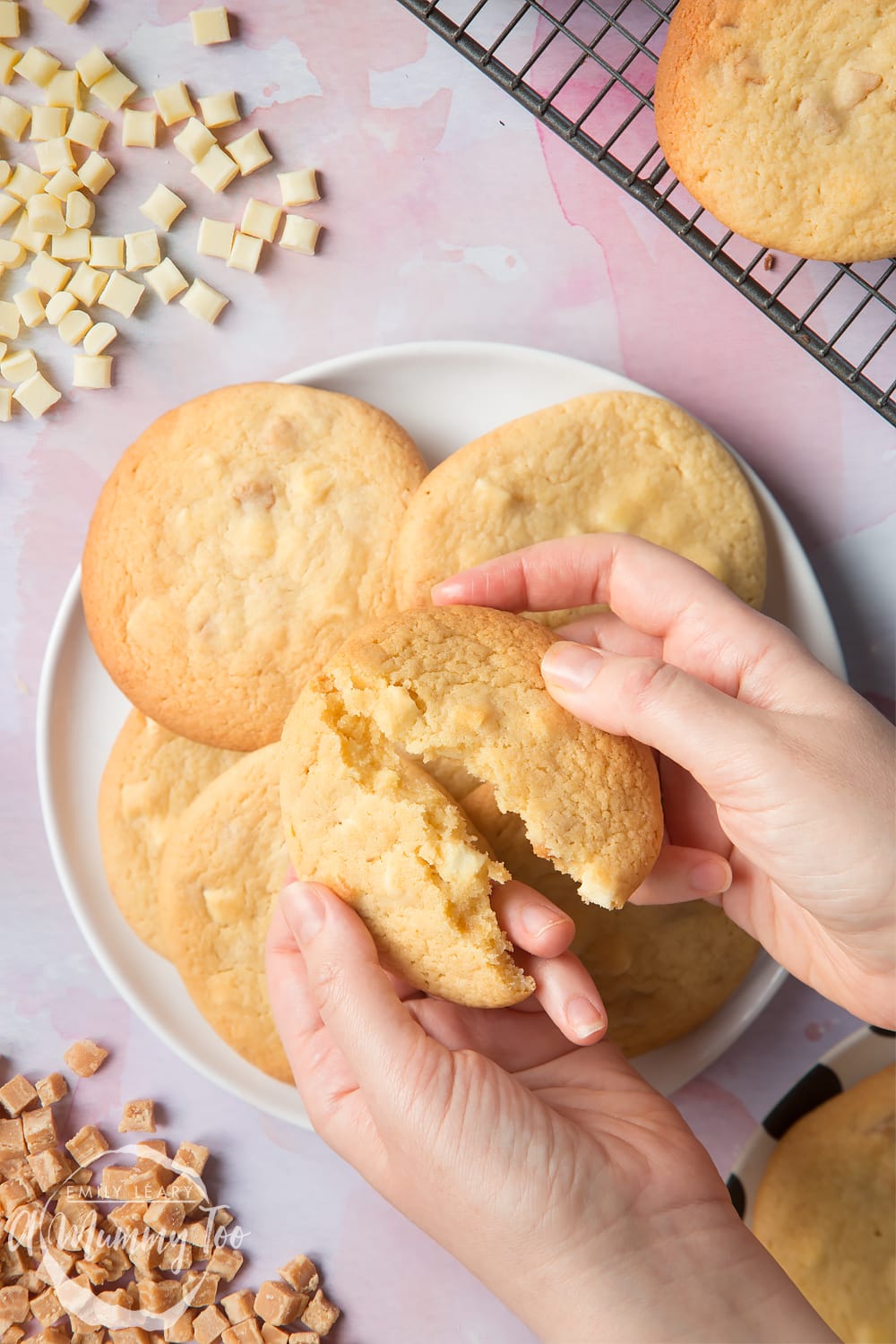 Overhead shot of a hand breaking a Fudge and white choc chip cookie open with a mummy too logo in the lower-left corner