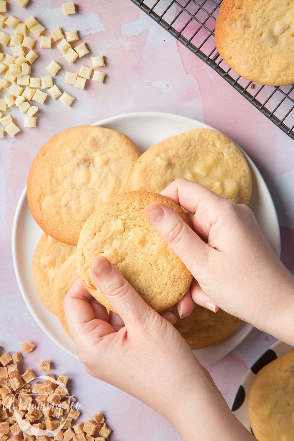 Overhead shot of a hands holding a Fudge and white chocolate chip cookie open with a mummy too logo in the lower-left corner