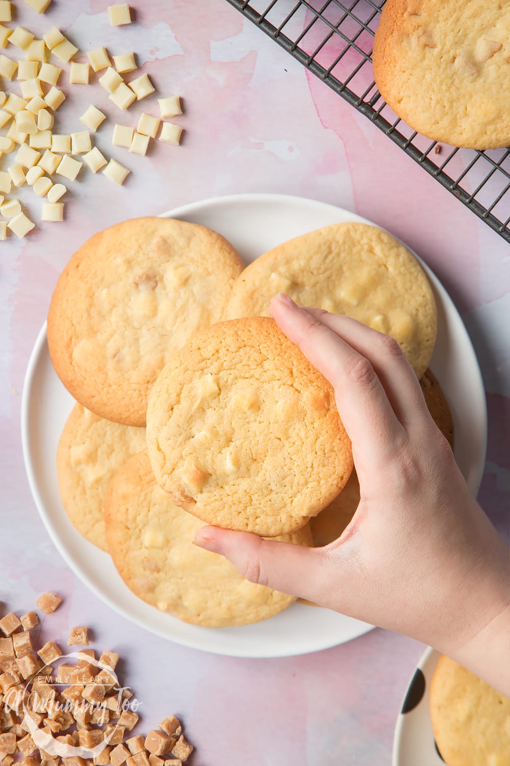 Overhead shot of a hand holding a Fudge and white chocolate chip cookie open with a mummy too logo in the lower-left corner