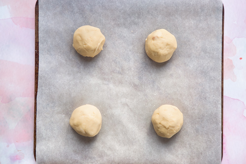 Overhead shot of four cookie dough balls in a paper-lined baking sheet