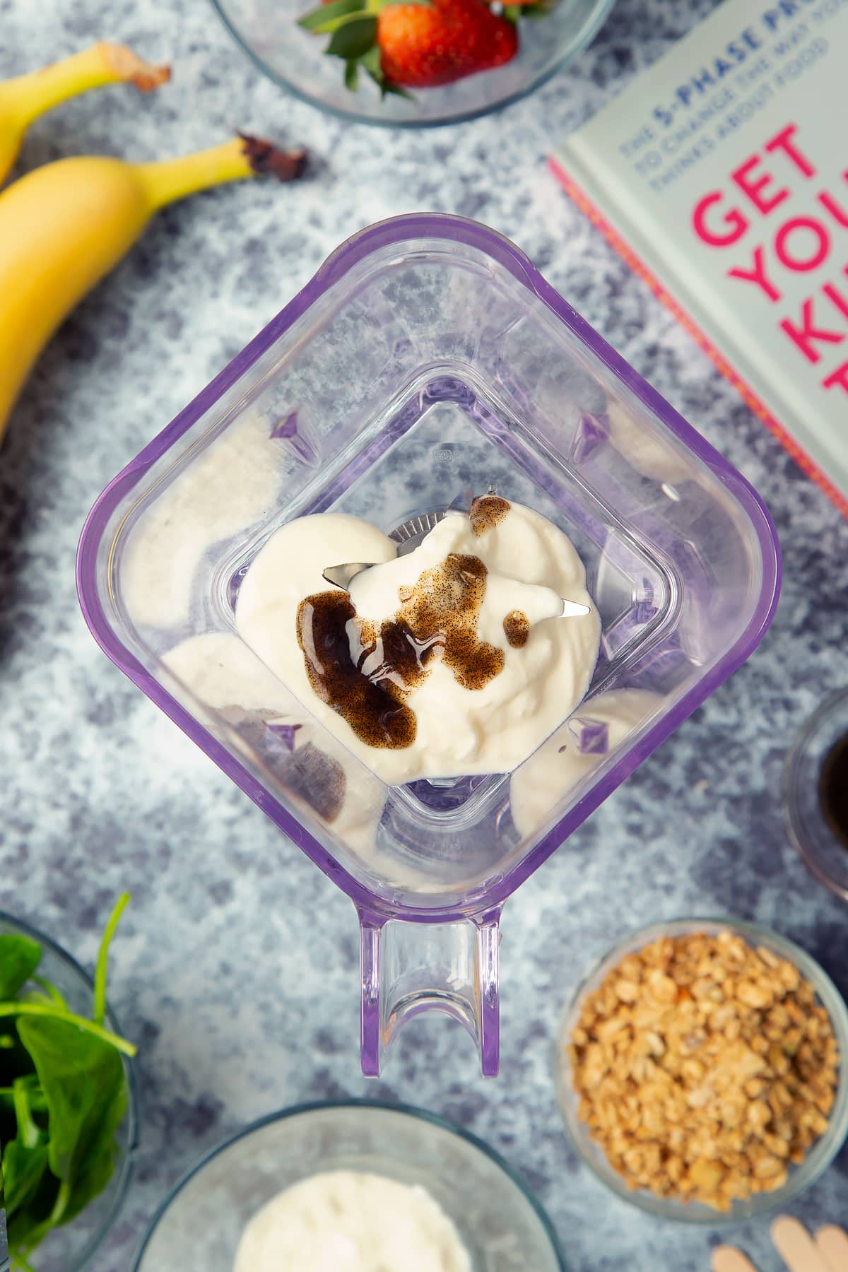 A blender is shown from above, containing yogurt and vanilla. The blender is surrounded by ingredients for fruit and veg lollies.