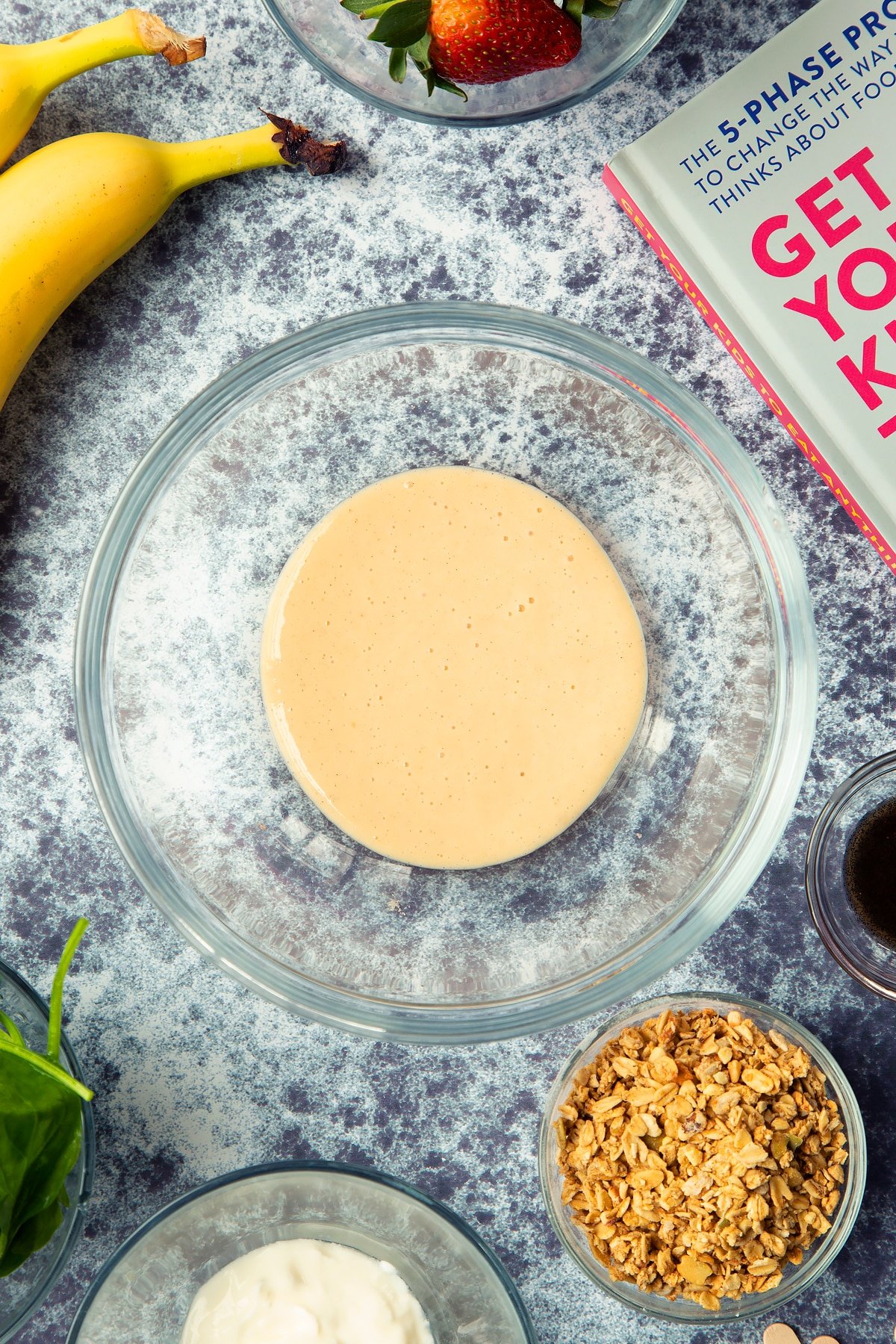 A bowl containing banana yogurt mix. The bowl is surrounded by ingredients for fruit and veg lollies.