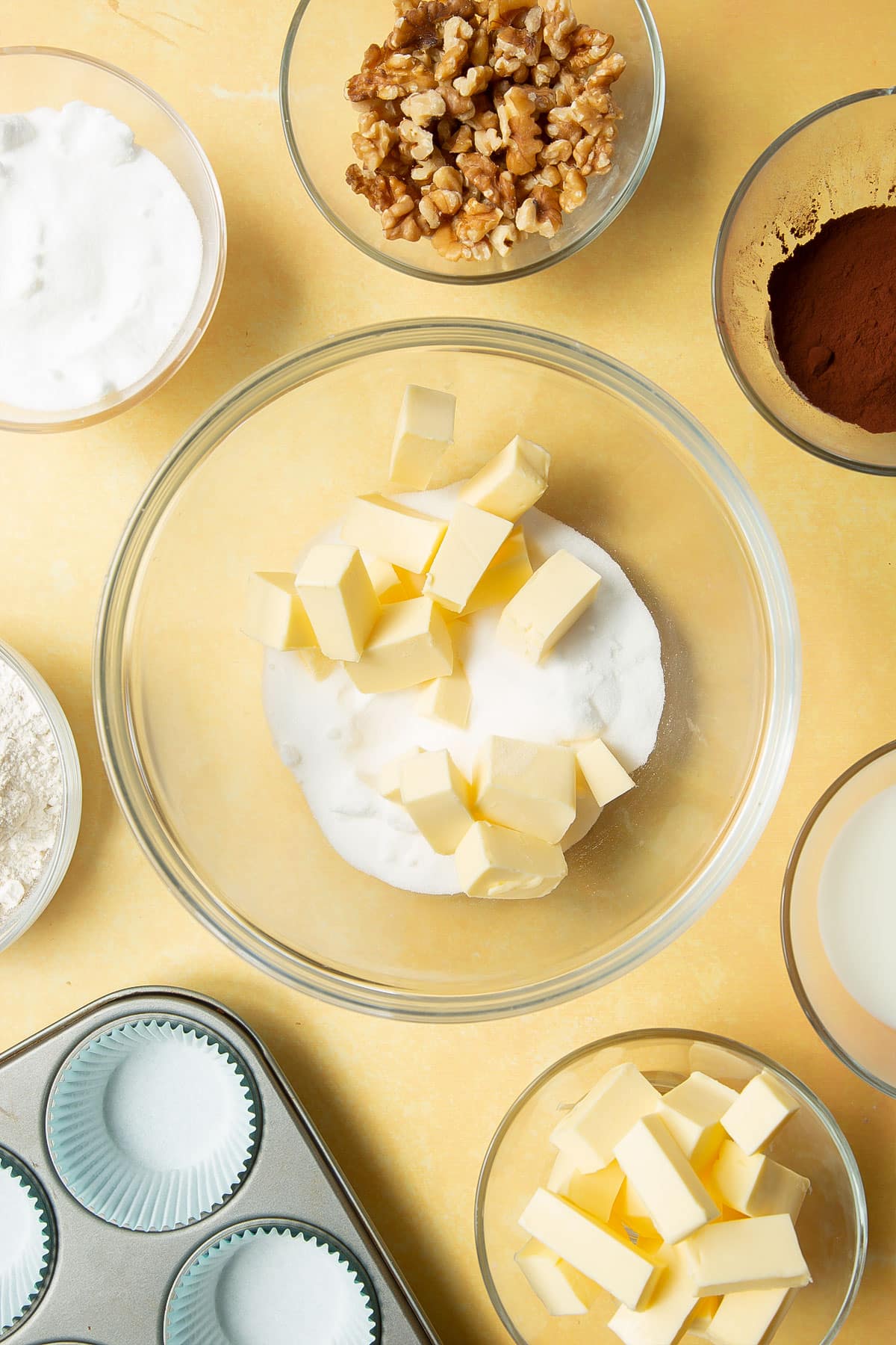 Butter and sugar in a glass mixing bowl. Ingredients for chocolate walnut cupcakes surround the bowl.