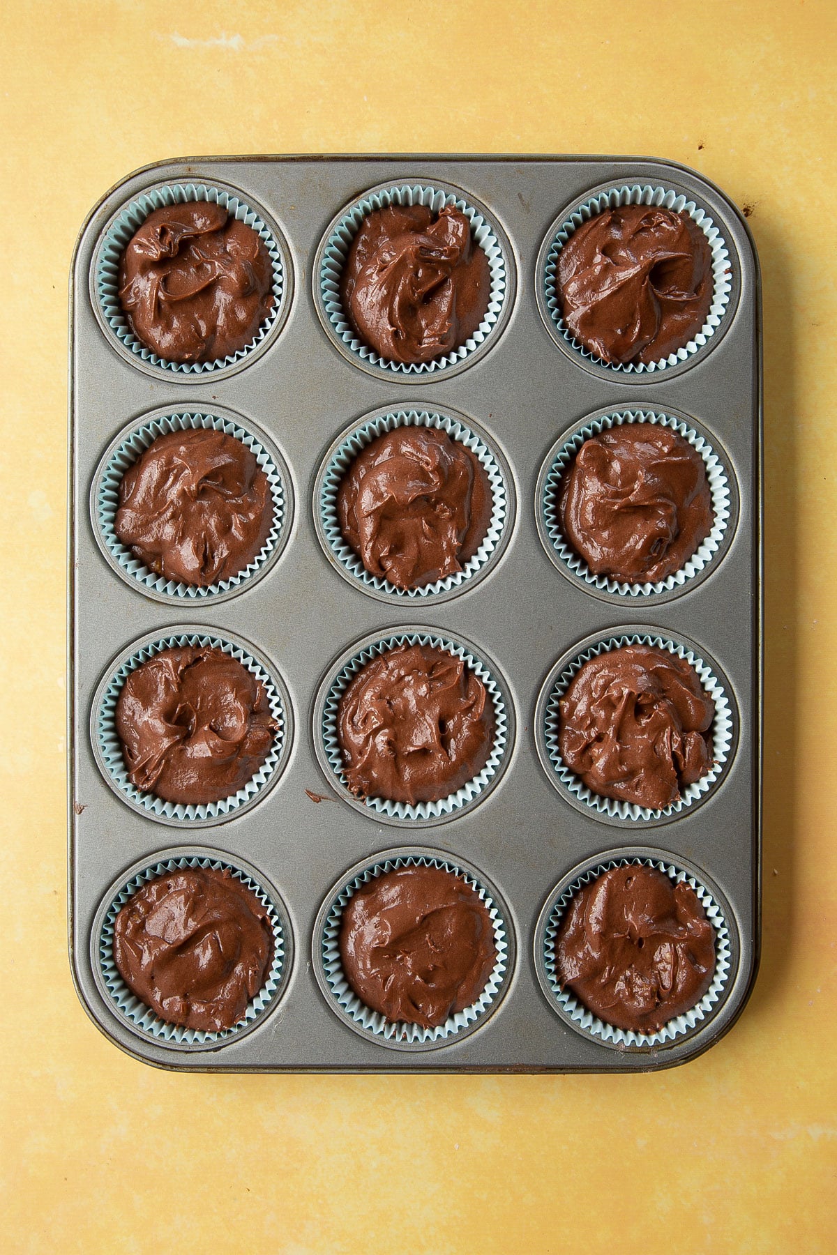 Chocolate walnut cupcake batter spooned into 12-hole muffin tray, lined with cupcake cases.