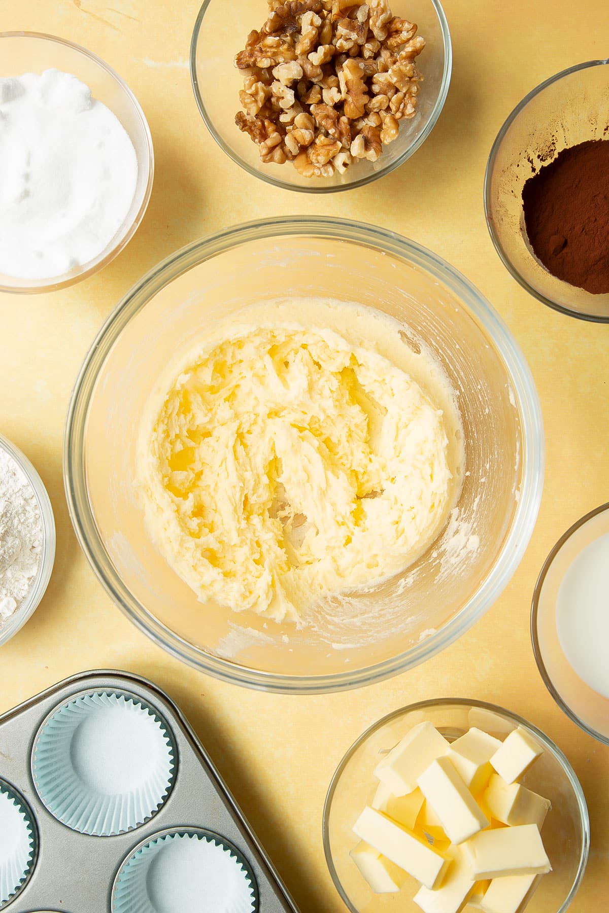 Butter and sugar, creamed together in a glass mixing bowl. Ingredients for chocolate walnut cupcakes surround the bowl.