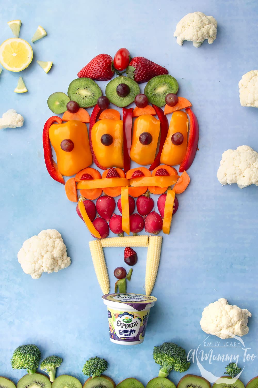 Overhead shot of a flatlay of fruit and vegetables in the shape of a hot air balloon flying in the sky.
