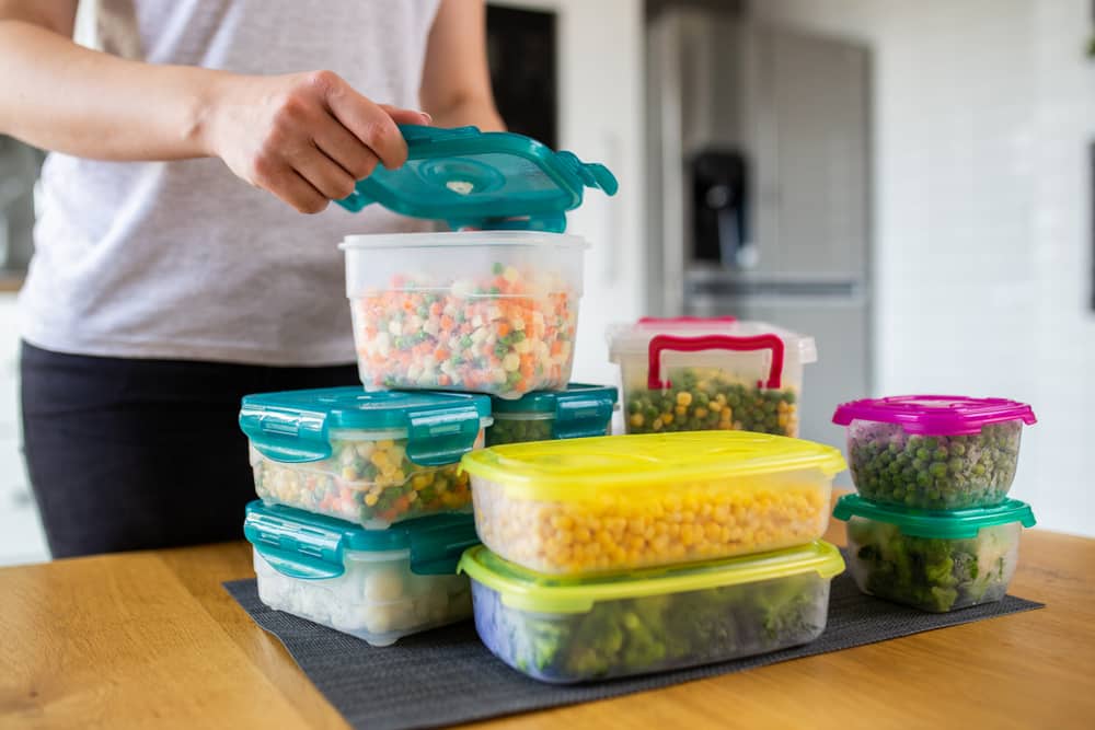 Pre-prepaired vegetables in plastic containers stacked on a table.