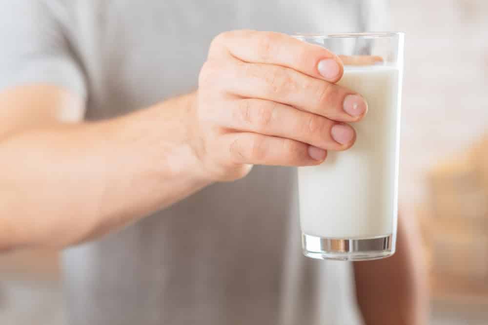 A hand holding a glass of soy milk.