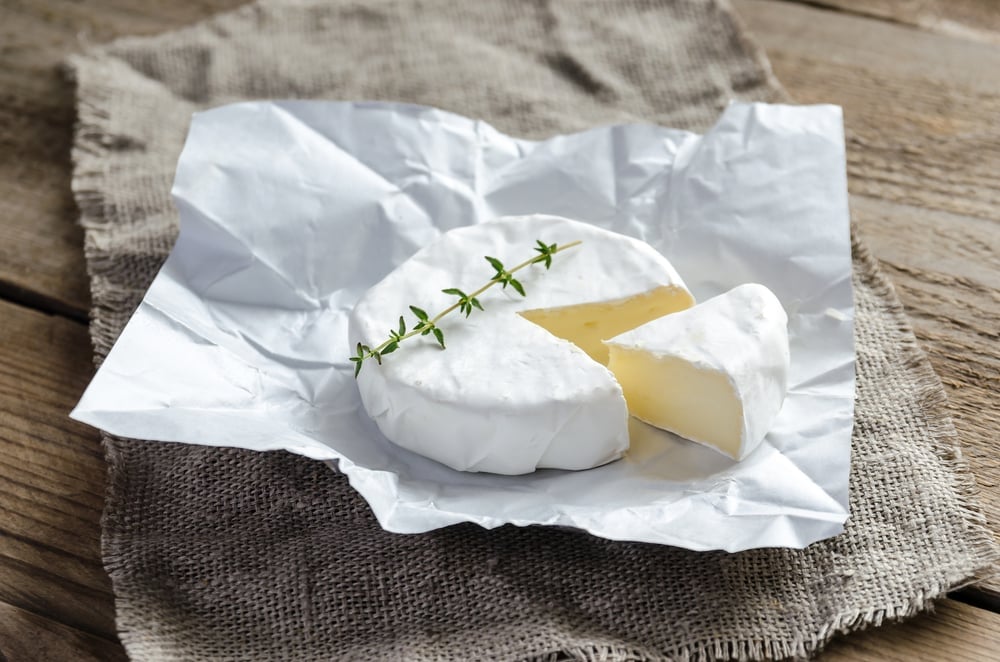 A sliced brie cheese unwrapped on a dark wooden table.