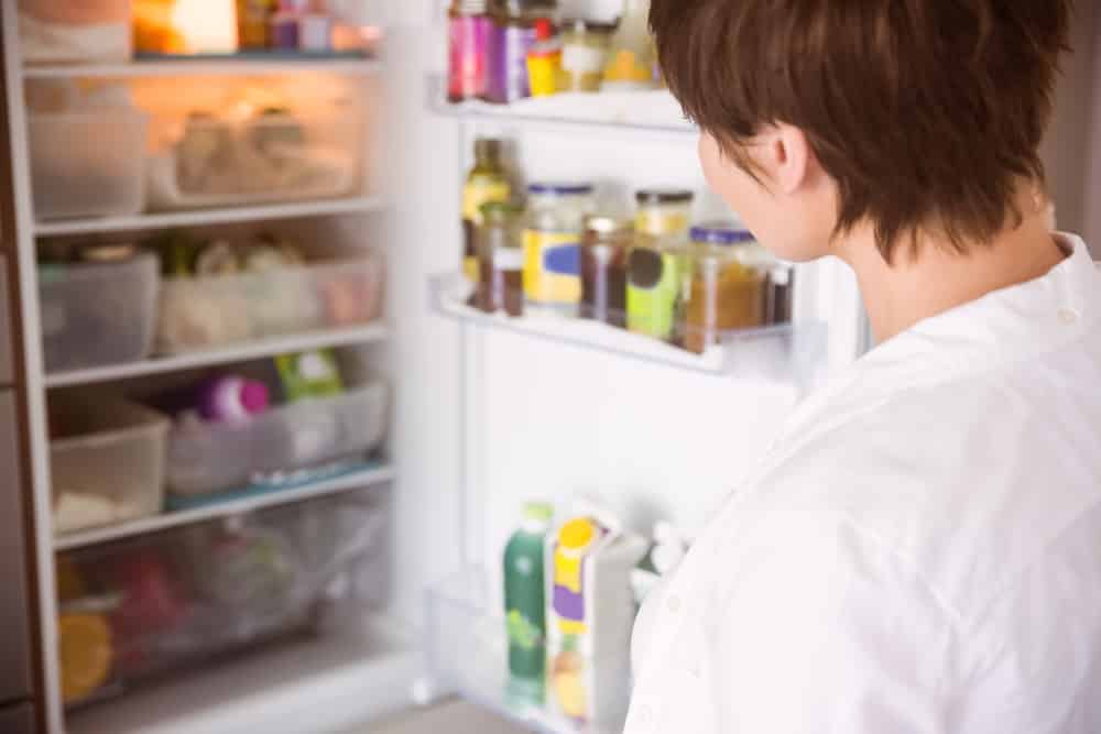 Woman opening a fridge filled with ingredients. 