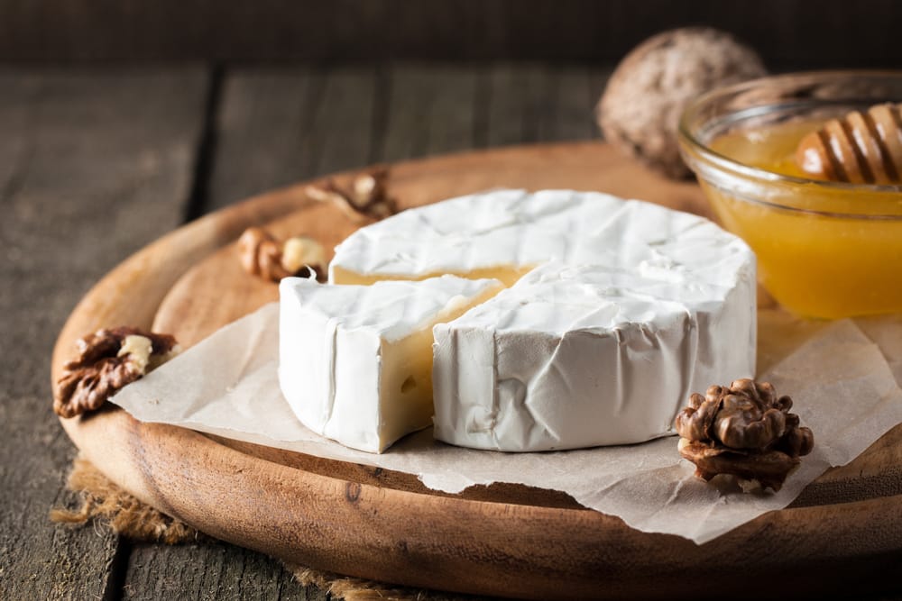 A sliced brie cheese on a wooden plate with a side of honey. 